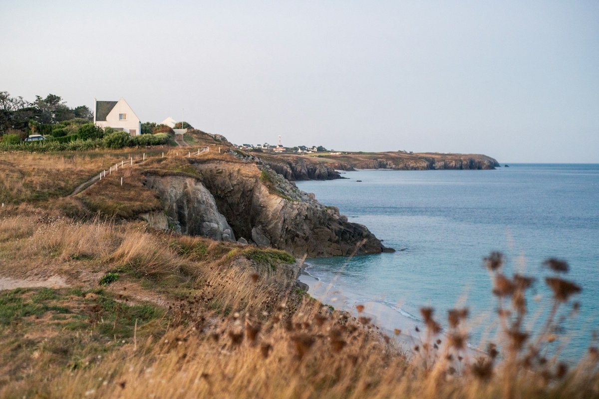 Côte rocheuse aux herbes sèches, mer bleue et maisons blanches au loin